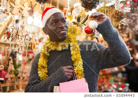 Guy in Santa hat choosing Christmas decorations 83894443