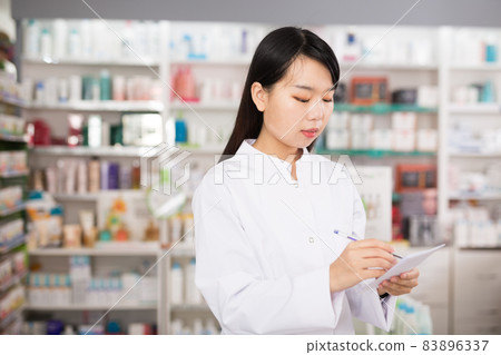 Chinese woman pharmacist keeps track of drugs in interior of pharmacy Chinese woman pharmacist keeps track of drugs in interior of pharmacy 83896337