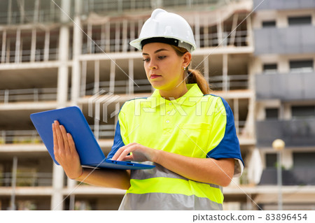 Woman architect standing with laptop in construction site Woman architect standing with laptop in construction site 83896454
