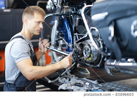 Male car mechanic holds wrench and looks at open motorcycle engine 83896603