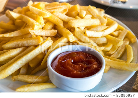 French fries in a white plate and ketchup on a table 83896957