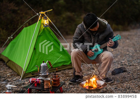 A man playing the ukulele in front of a bonfire 83899458