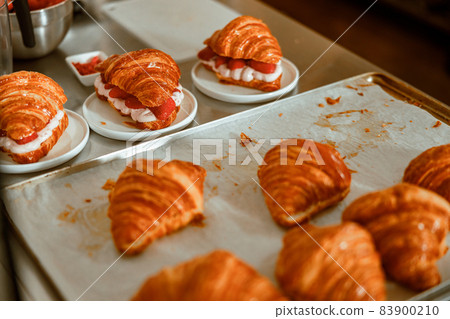 Croissants with cream and fresh strawberries on metal table in shop 83900210