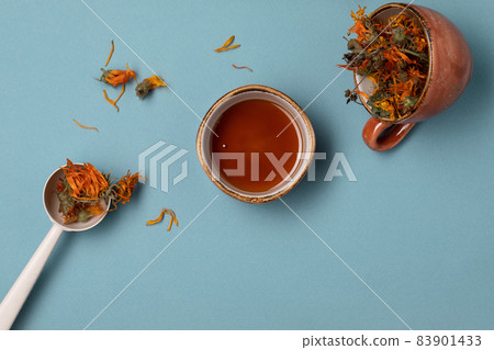 Calendula dried herbs in orange craft cup with honey on blue background Calendula dried herbs in orange craft cup with honey on blue background 83901433