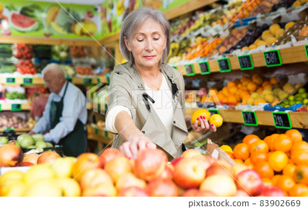 Old lady choosing fruits in greengrocer Old lady choosing fruits in greengrocer 83902669