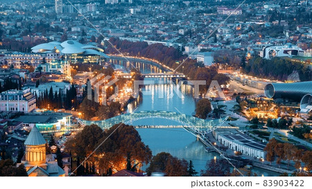 Tbilisi, Georgia. Top View Of Famous Landmarks In Night Illuminations. Georgian Capital Skyline Cityscape. City During Sunset And Night Illuminations. Day To Night Transition Tbilisi, Georgia. Top View Of Famous Landmarks In Night Illuminations. Georgian Capital Skyline Cityscape. City During Sunset And Night Illuminations. Day To Night Transition 83903422