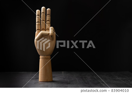 Picture of a wooden hand showing hand signal. The hand is placed on a wooden table with black background Picture of a wooden hand showing hand signal. The hand is placed on a wooden table with black background 83904010