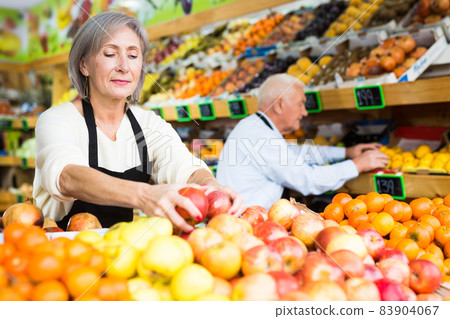 Mature man and woman supermarket workers setting out fruits Mature man and woman supermarket workers setting out fruits 83904067