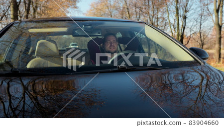 Emotional man in car, view through windshield. Aggressive driving behavior. Angry man driver hitting the steering wheel with his fists. 83904660