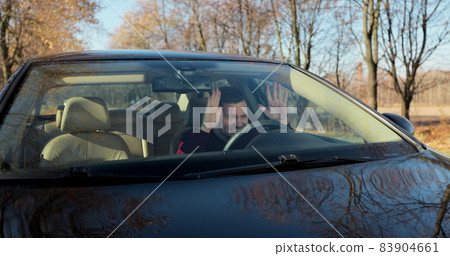 Emotional man in car, view through windshield. Aggressive driving behavior. Angry man driver hitting the steering wheel with his fists. 83904661