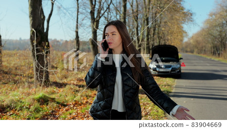 Young stressed woman calling for assistance with her car broken down by the roadside. Helpless woman need help and assistance. 83904669