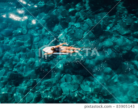 Surfer woman rowing on surfboard in turquoise ocean. Aerial view with surfgirl Surfer woman rowing on surfboard in turquoise ocean. Aerial view with surfgirl 83905143
