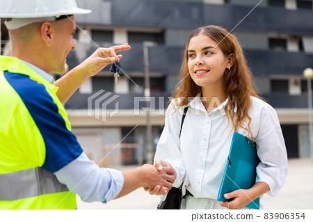 Builder giving keys to woman in construction site 83906354