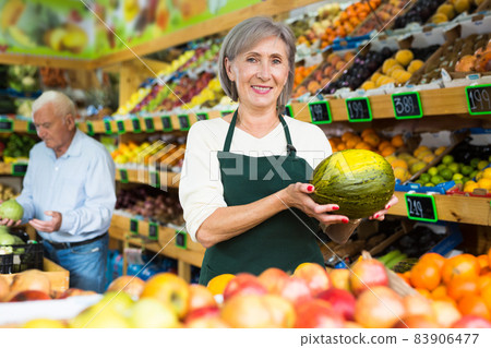Portrait of positive supermarket worker with fresh ripe watermelon from counter at market Portrait of positive supermarket worker with fresh ripe watermelon from counter at market 83906477