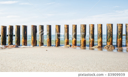 Wooden breakwater on the sandy shore, washed by the waves against the background of the sea Wooden breakwater on the sandy shore, washed by the waves against the background of the sea 83909939