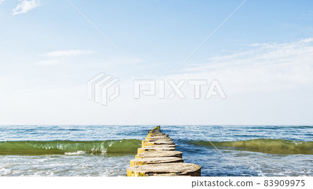 A bird sits in the distance on a wooden breakwater in a rough sea A bird sits in the distance on a wooden breakwater in a rough sea 83909975