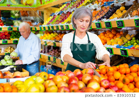 Woman merchandiser in apron putting goods on shelf in supermarket 83910332