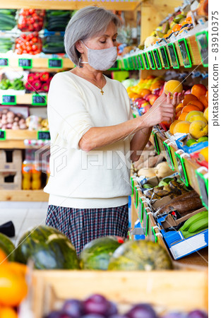 Woman in mask choosing peaches in supermarket Woman in mask choosing peaches in supermarket 83910375