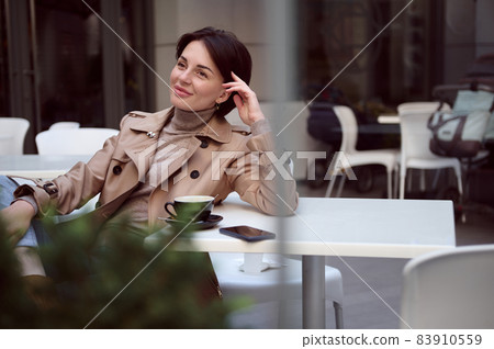 Daydreaming. Happy fashionable elegant young woman resting on summer terrace of summer cafeteria enjoying warm sunny autumn weather during coffee break 83910559