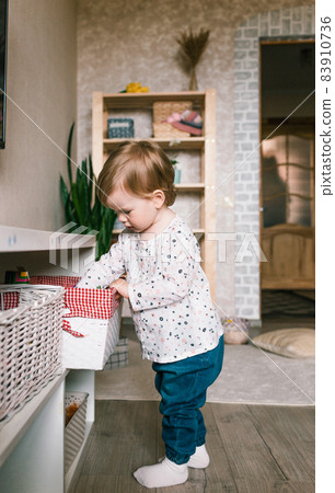 a little girl picks out a toy in a large white basket standing on the floor 83910736
