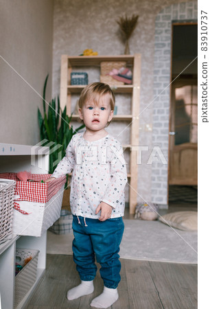a little girl picks out a toy in a large white basket standing on the floor 83910737