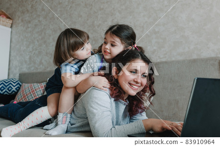two little girls sit on their mother's back while working on the computer two little girls sit on their mother's back while working on the computer 83910964