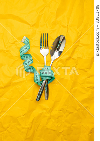 Steel spoon a fork and measuring tape on yellow paper texture background 83911788