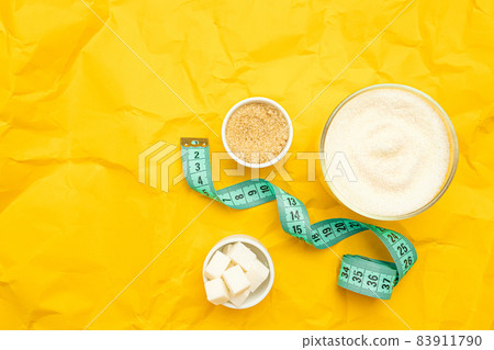 Different types of sugar and diet measuring tape on yellow background with copy space. Weight control, healthy food, diet. 83911790