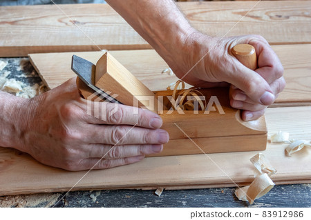 Men's hands hold a wooden jointer close-up. Light wood boards, shavings, sawdust Men's hands hold a wooden jointer close-up. Light wood boards, shavings, sawdust 83912986
