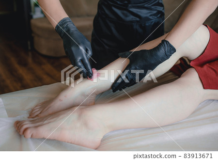 Carrying out the depilation procedure . A confident professional depilation master is preparing to apply wax to the client's feet 83913671