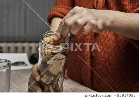 A person making banana peel fertilizer with banana cuts. Putting small pieces of banana skin into the glass jar and pouring water 83914083