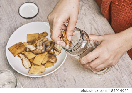A person making banana peel fertilizer with banana cuts. Putting small pieces of banana skin into the glass jar and pouring water 83914091
