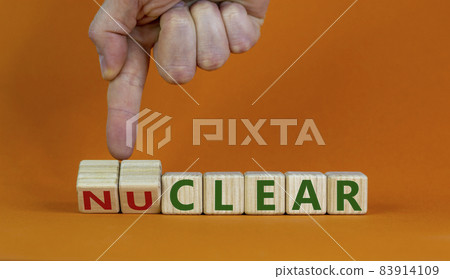 Nuclear or clear symbol. Businessman turns a cube and changes the word 'nuclear' to 'clear'. Beautiful orange background. Nuclear or clear and business concept. Copy space. Nuclear or clear symbol. Businessman turns a cube and changes the word 'nuclear' to 'clear'. Beautiful orange background. Nuclear or clear and business concept. Copy space. 83914109