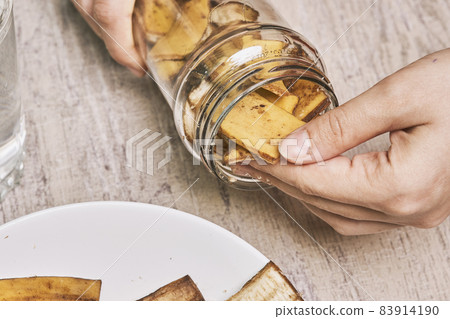 A person making banana peel fertilizer with banana cuts. Putting small pieces of banana skin into the glass jar and pouring water 83914190