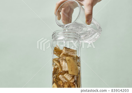 A person making banana peel fertilizer with banana cuts. Putting small pieces of banana skin into the glass jar and pouring water 83914203