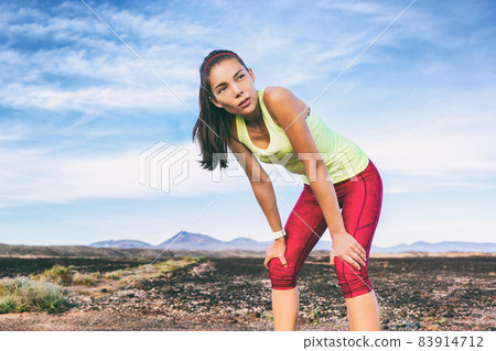 Tired runner girl taking a break breathing during jogging training workout outdoor on desert trail. Asian woman sweating in summer heat. 83914712