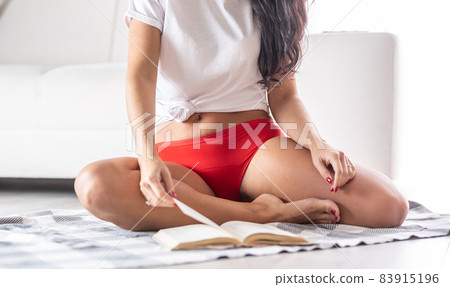 Detail of a woman wearing red period underwear sitting comfortably on the floor, reading a book Detail of a woman wearing red period underwear sitting comfortably on the floor, reading a book 83915196