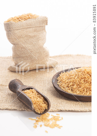 Brown rice on wooden plate and spoon and burlap sack on white backround. Brown rice on wooden plate and spoon and burlap sack on white backround. 83915891