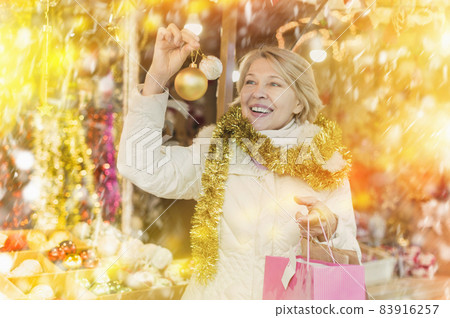 Woman is preparing for Christmas and choosing balls on the tree Woman is preparing for Christmas and choosing balls on the tree 83916257