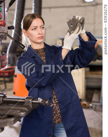 Workwoman drilling metal parts on bench drill Workwoman drilling metal parts on bench drill 83916278