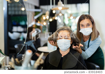 Elderly woman in protective mask sitting in chair of hairstylist 83918403