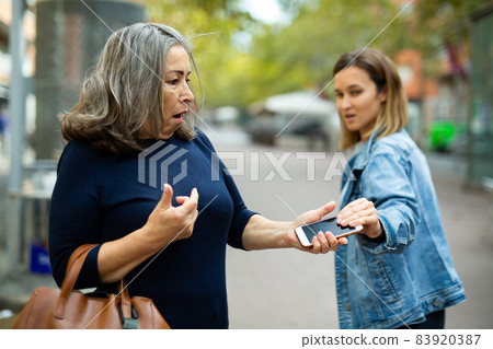Female thief trying to snatch phone of elderly woman outdoors Female thief trying to snatch phone of elderly woman outdoors 83920387