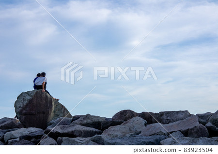 Image of youth and friendship between two people sitting on a big rock Image of youth and friendship between two people sitting on a big rock 83923504