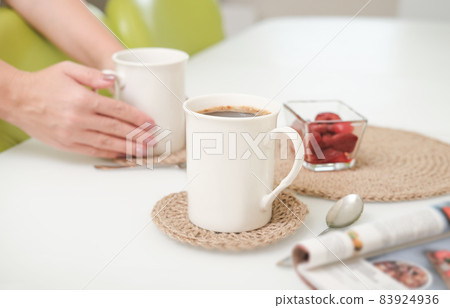 woman serving a coffee in a white light kitchen using eco knit jute tablemats. good morning concept. crop view. 83924936