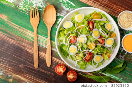 Big white bowl of lettuce, sprout salad with boil egg, and tomato mix with sesame dressing above wooden table with wooded utensil, small olive oil jar and sesame cup. Concept for healthy Big white bowl of lettuce, sprout salad with boil egg, and tomato mix with sesame dressing above wooden table with wooded utensil, small olive oil jar and sesame cup. Concept for healthy 83925520