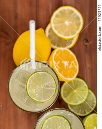 A close up picture of refreshing glasses of cold fruit juice with straw, ice lime and lemon juice, decorating with fresh lime and lemon on wooden table. Concept for refreshing A close up picture of refreshing glasses of cold fruit juice with straw, ice lime and lemon juice, decorating with fresh lime and lemon on wooden table. Concept for refreshing 83925733