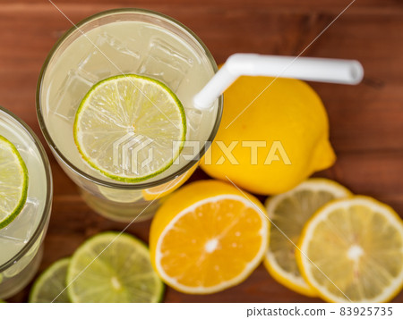 A close up picture of two refreshing glasses of cold fruit juice with straw, ice lime and lemon juice, decorating with fresh lime and lemon on wooden table. Concept for refreshing A close up picture of two refreshing glasses of cold fruit juice with straw, ice lime and lemon juice, decorating with fresh lime and lemon on wooden table. Concept for refreshing 83925735