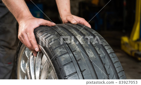 An auto mechanic holds a wheel of a car. Change of car tires according to the season 83927053