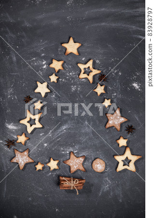 Homemade cookies in shape of stars, cinnamon and anise stars laid out in form of Christmas tree on black textured backdrop. Christmas festive baking creative mock up. Top view, flat lay. Copy space. 83928797