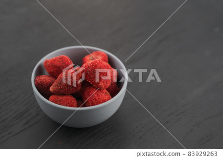 Freeze dried strawberries in blue bowl on black wood table 83929263